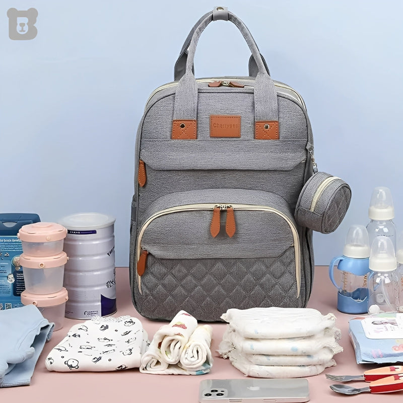 Gray diaper bag with baby care items on a pink surface against a light blue background