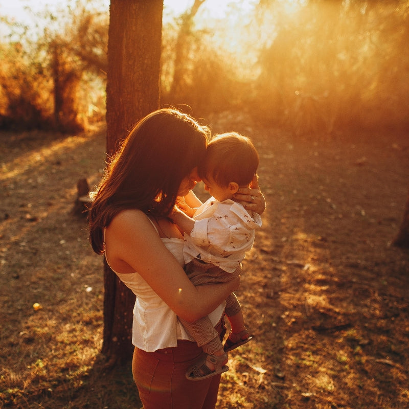 Woman holding a child in a forest during sunset