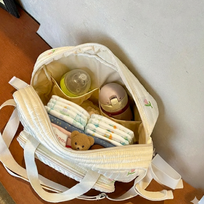 Open baby bag with diapers, bottles, and a teddy bear on a wooden surface.