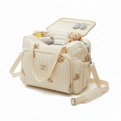 Beige quilted diaper bag with teddy bear and baby items on a white background