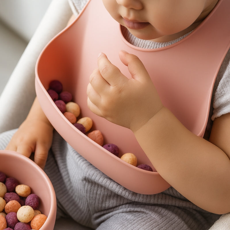 Child wearing a pink bib with colorful berries, sitting on a light-colored surface.
