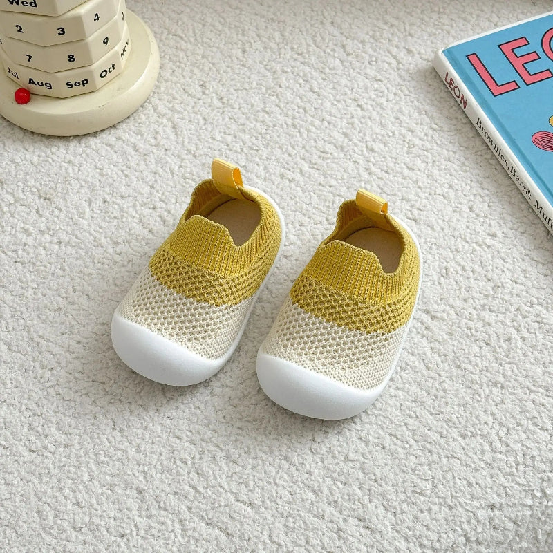 Yellow baby shoes on a textured surface with a book and calendar in the background