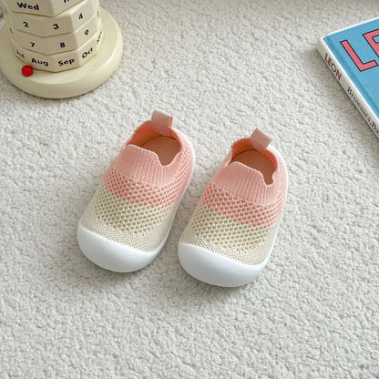Pair of pink and beige baby shoes on a textured surface with a calendar and book in the background.