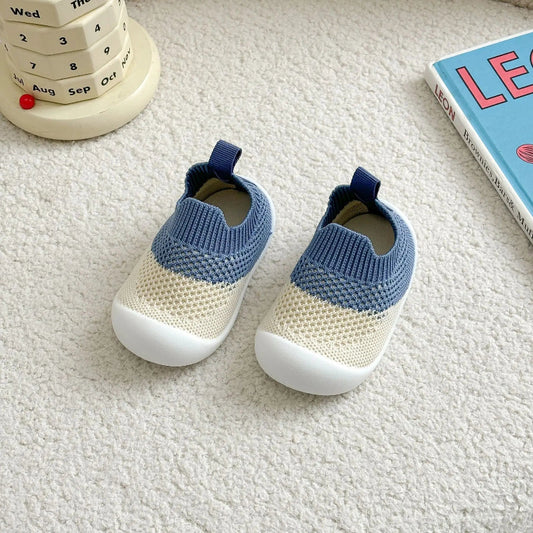 Pair of blue and beige baby shoes on a textured surface with a book and calendar in the background.