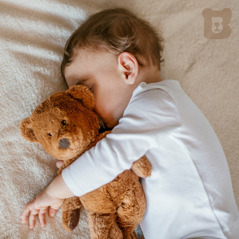 Child sleeping with a teddy bear on a soft surface